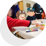 a group of children sitting at a table with an adult wearing a mask